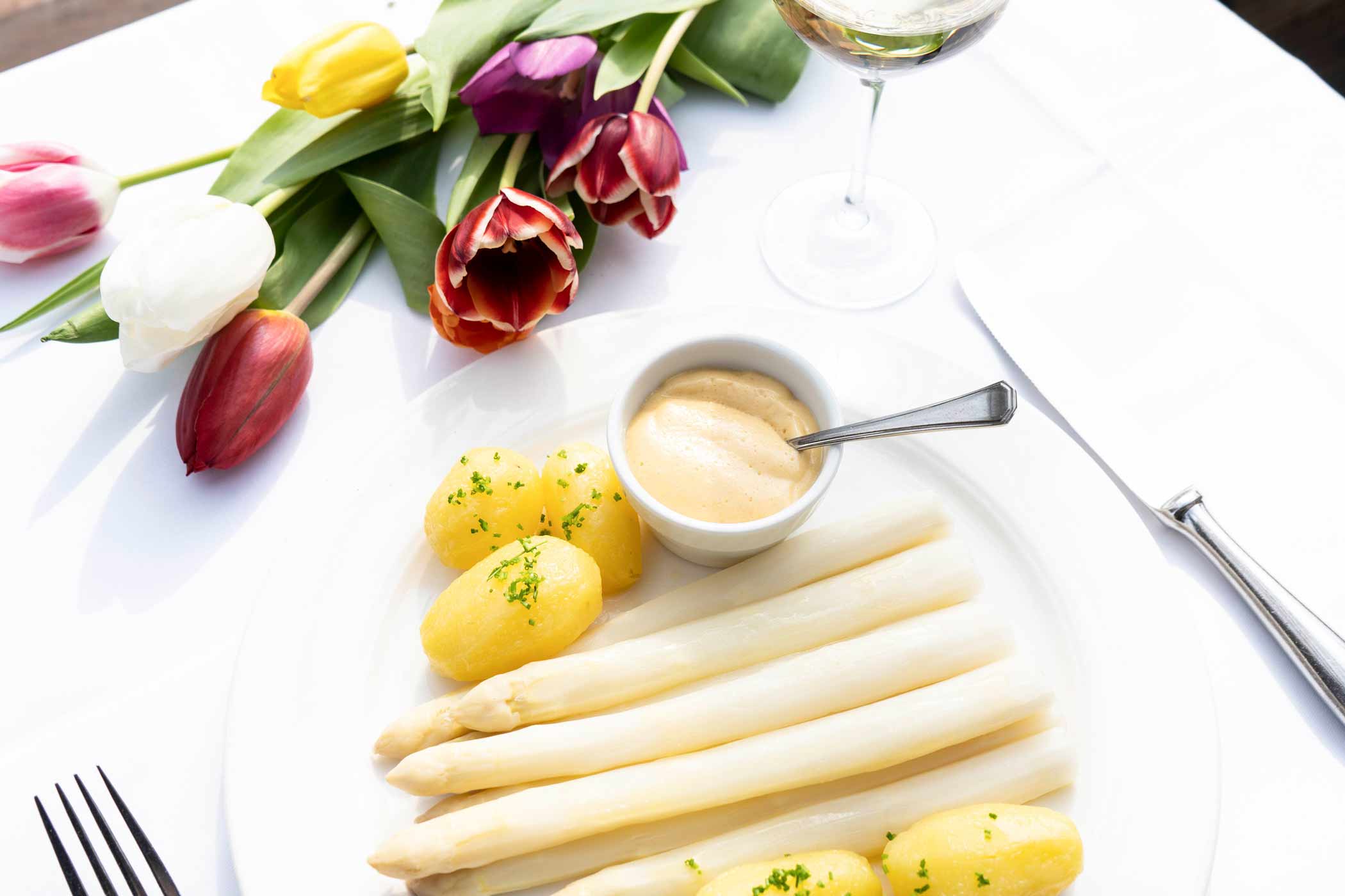 Gekochter Spargel mit Kartoffeln uns Sauce Hollandaise auf einem frühlingshaft gedecktem Tisch