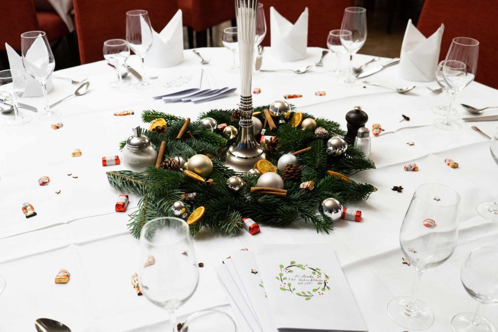 Festlich dekorierter Saal mit Weihnachtsbeleuchtung und gedeckten Tischen.