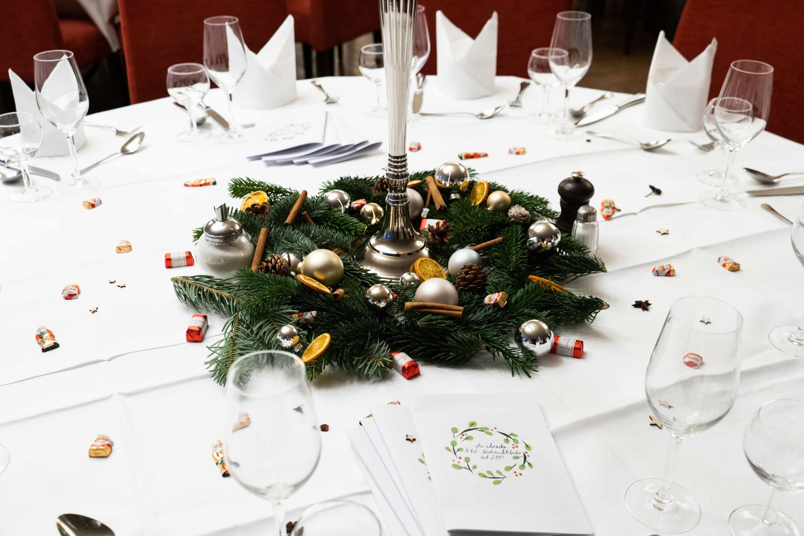 Festlich dekorierter Saal mit Weihnachtsbeleuchtung und gedeckten Tischen.
