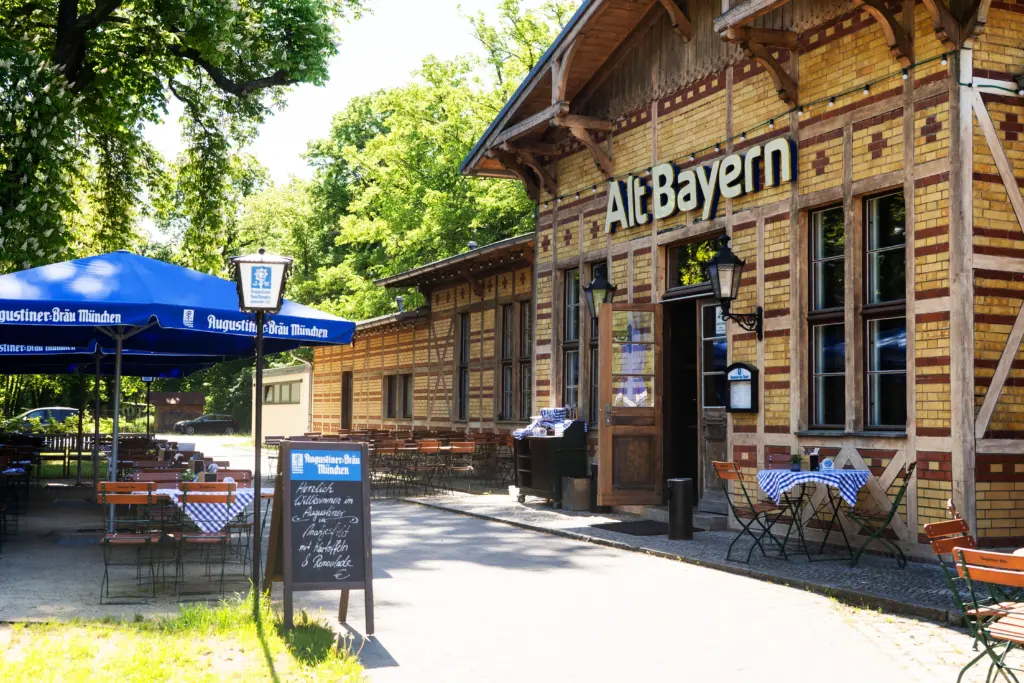 Seitliche Ansicht der Fassade des Bürgerbahnhofs. Historisches Backsteingebäude  mit gemütlichen Biergarten unter blauen Sonnenschirmen und einem Menü-Aufsteller im Vordergrund.