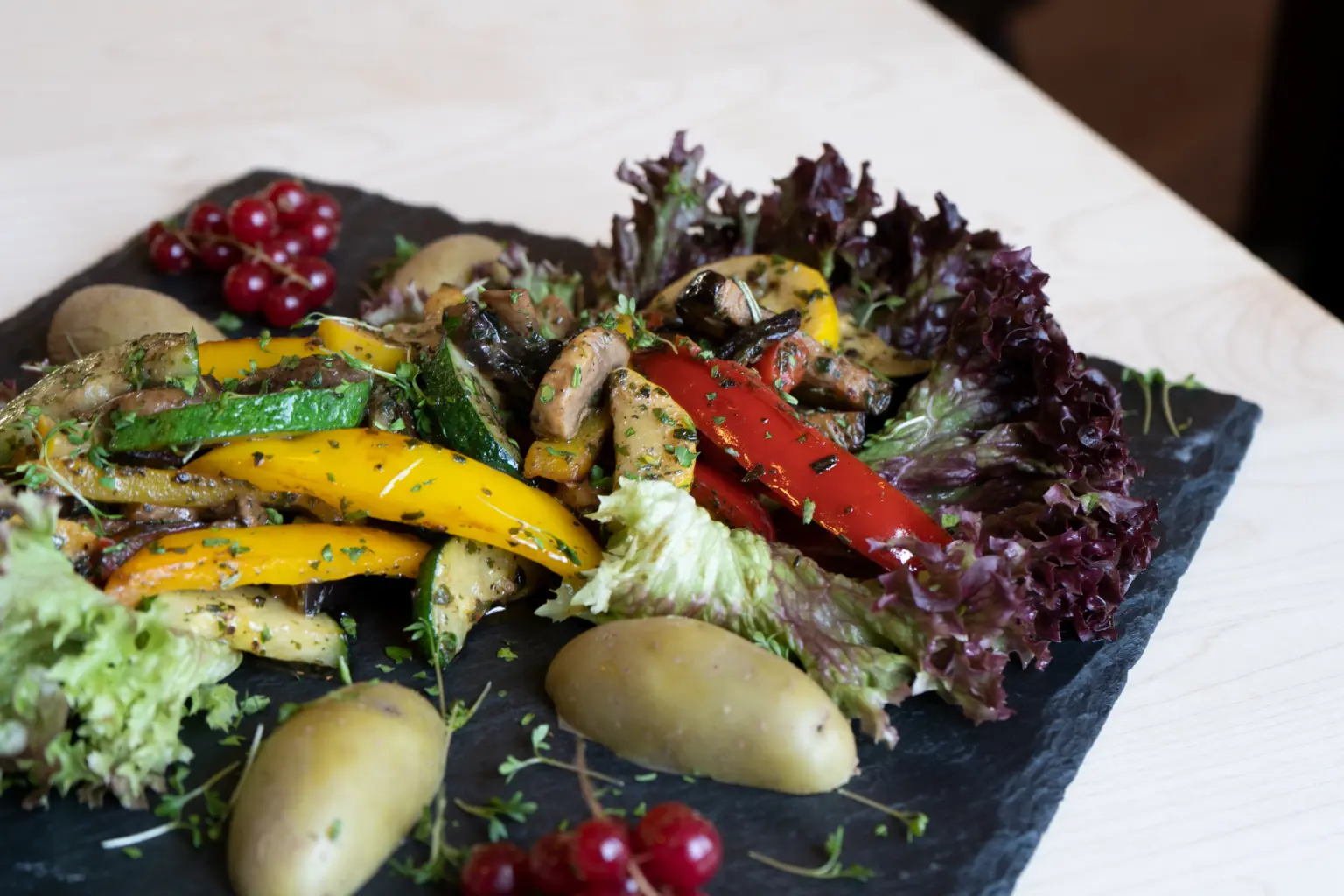 Gegrilltes und frisches Gemüse dekorativ angerichtet mit Salat auf einer edlen, dunklen Schieferplatte.
