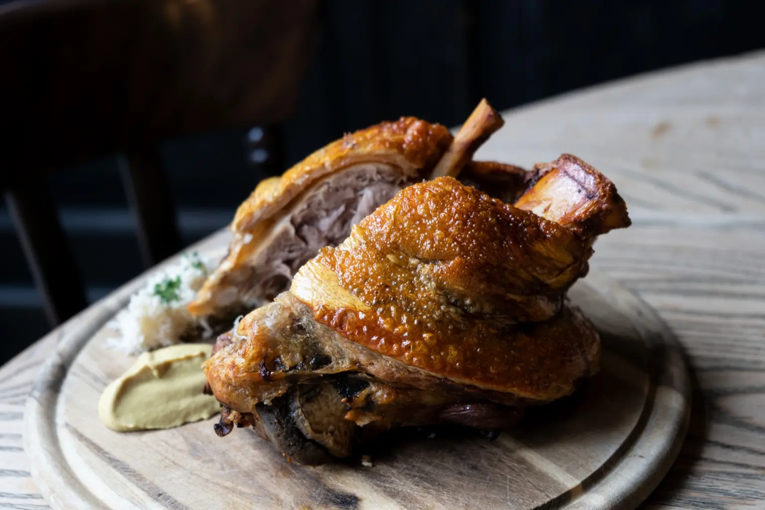Kross gegarte Schweinshaxe serviert auf einem Holzbrett mit Garnitur.