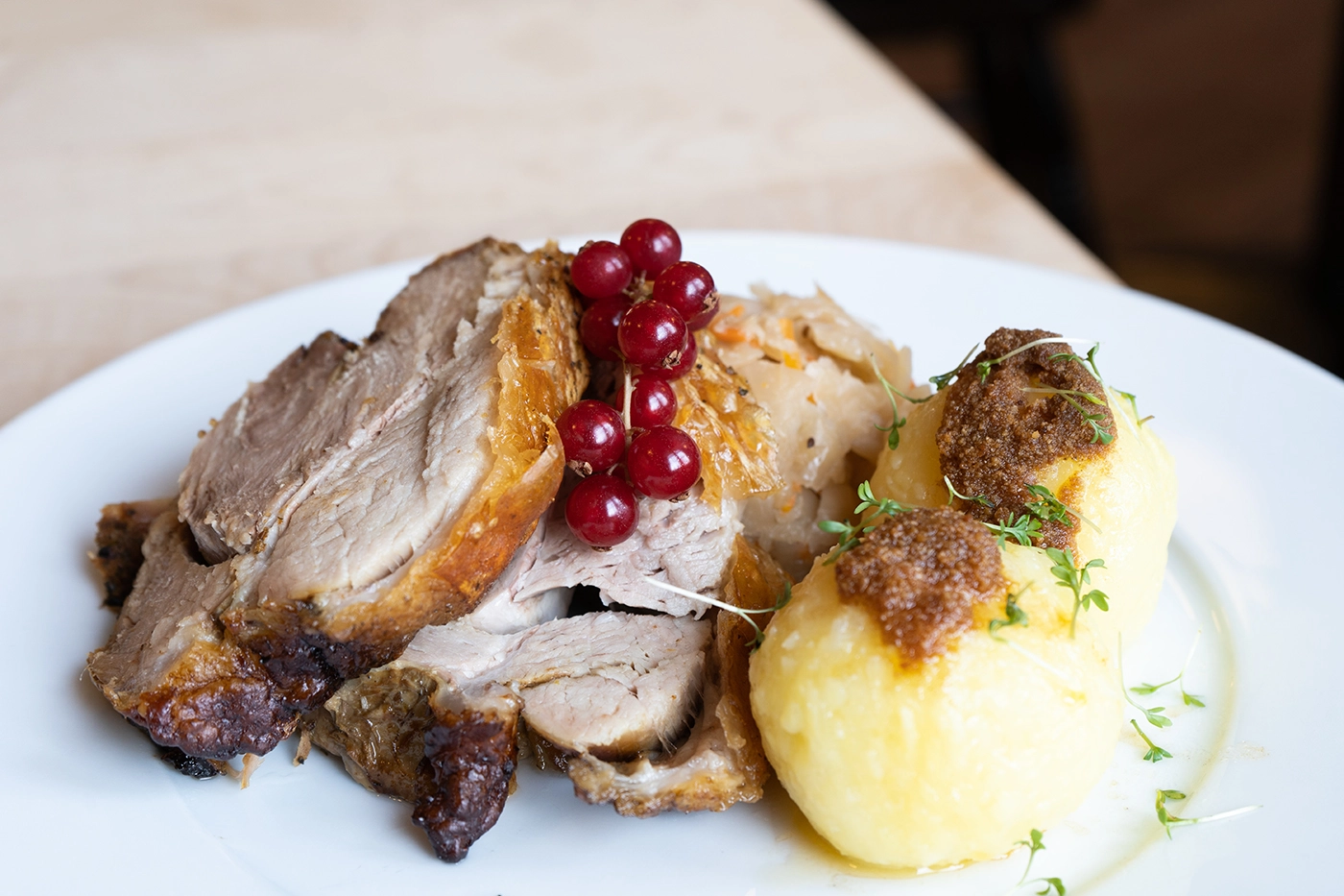 Traditioneller Schweinsbraten mit knuspriger Kruste, serviert mit Sauce und Beilagen auf einem Teller in Querformat.