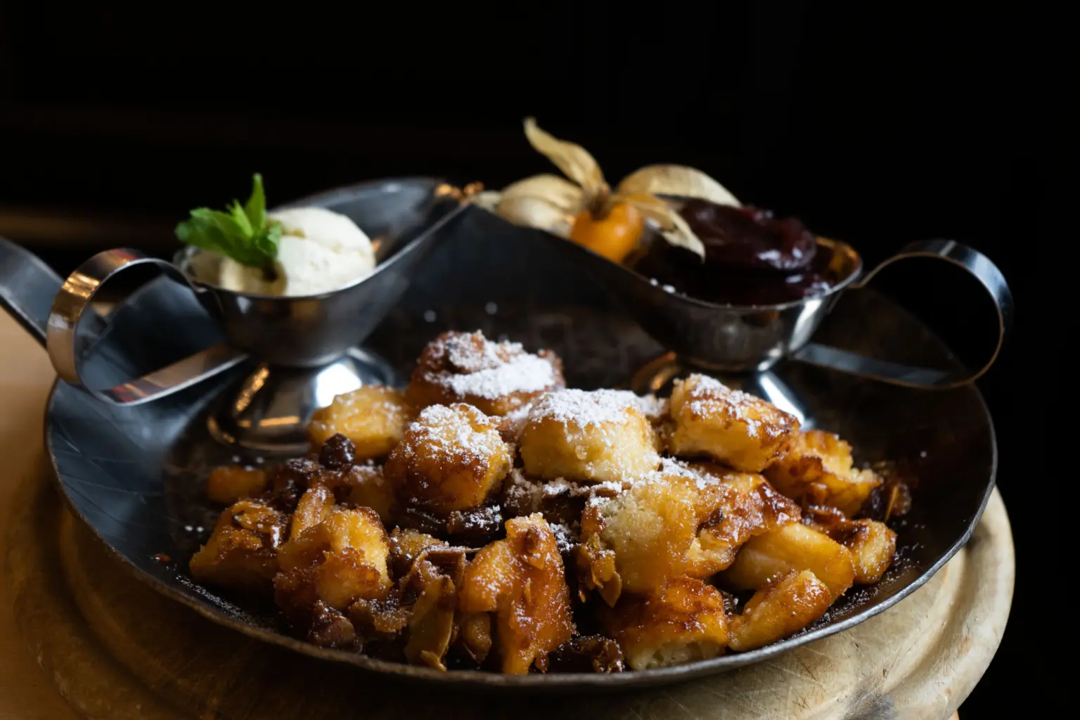 Traditioneller, mit Puderzucker bestreuter Kaiserschmarrn in einer rustikalen Eisenpfanne, serviert mit Zwetschgenröster.