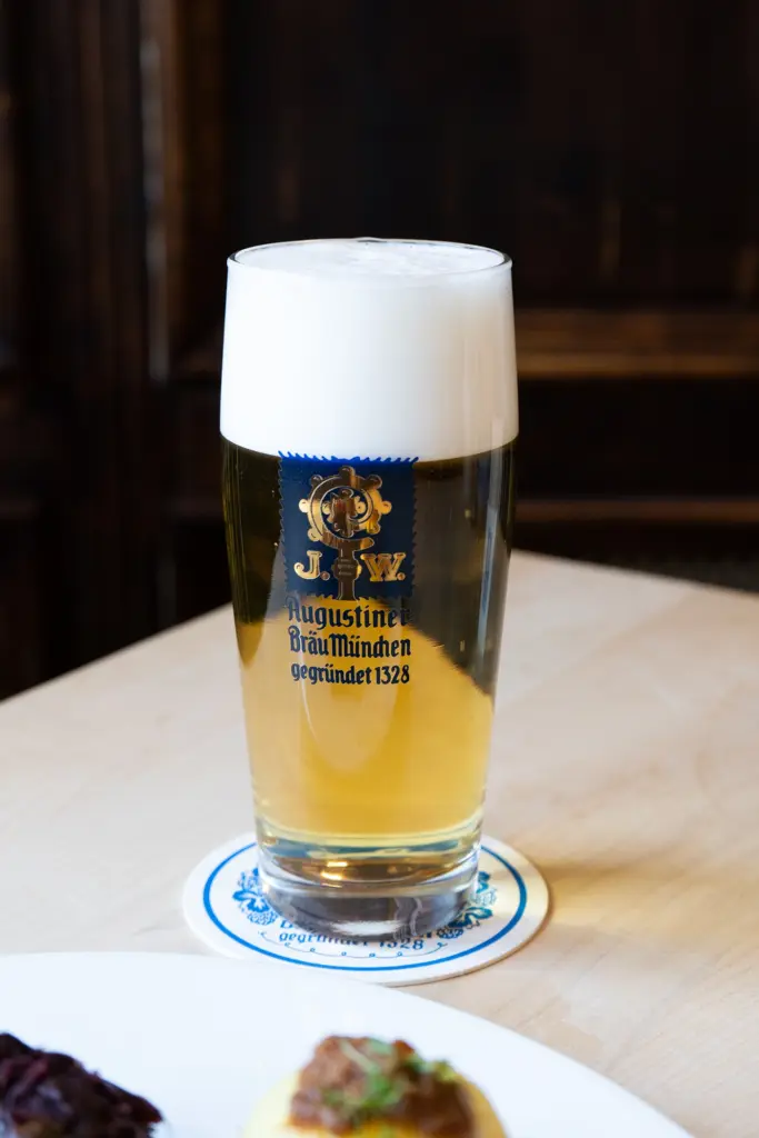 Augustiner Hell Bier auf hellem Hintergrund, klassisches Münchner Lagerbier in grüner Glasflasche.