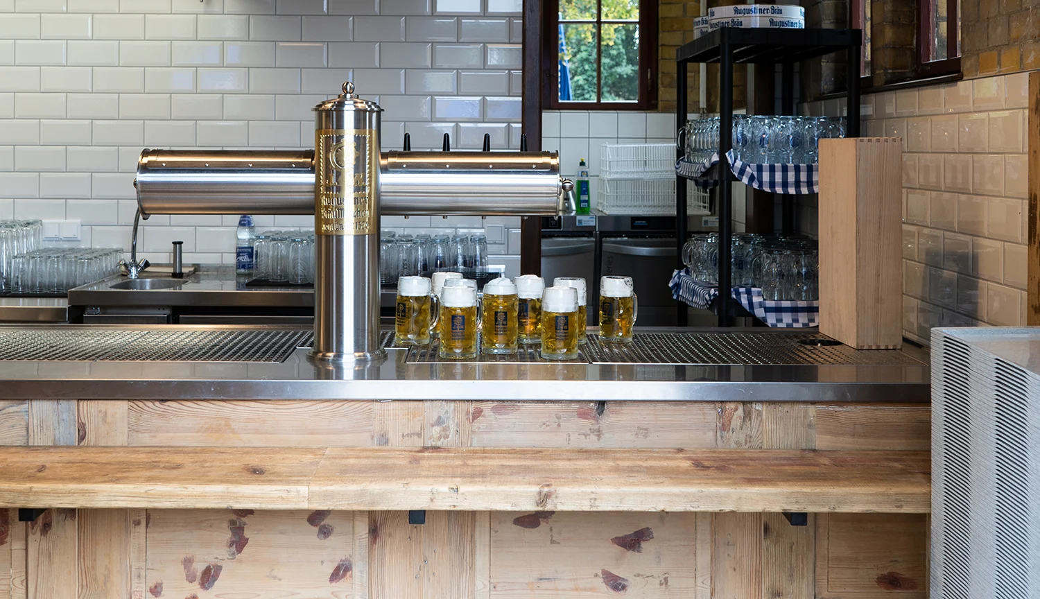 Frisch gezapfte Biere mit weißer Schaumkrone stehen aufgereiht an einer Schankanlage auf einem hölzernen Tresen im Ausschankbereich.